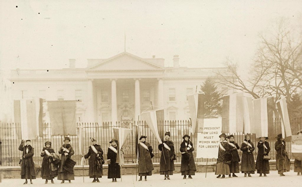 A group of women stand in front of the White House protesting, circa 1917