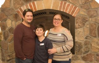 Bill, Adam, and Carrie stand in front of a fireplace