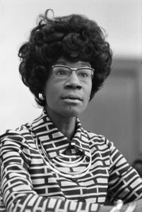 Black & white image of Shirley Chisholm looking ahead and slightly to the right of the viewer. Link to event registration.