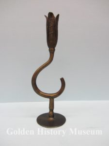 One of a matching pair of iron candlesticks hand forged by Golden blacksmith Henry Oldag. Bottom of candlestick is stamped H. Oldag, Golden, 1934. His shop was located on Washington Avenue and was called the Avenue Blacksmith Shop. The candle holder portion looks like a tulip with the shaft portion shaped like a hook.