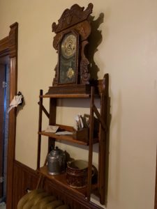 Wooden wall mounted shelf with various items including a clock on the top shelf.