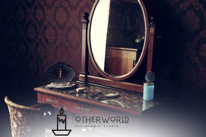 Vintage vanity table with an oval mirror and ornate chair in a dimly lit room.