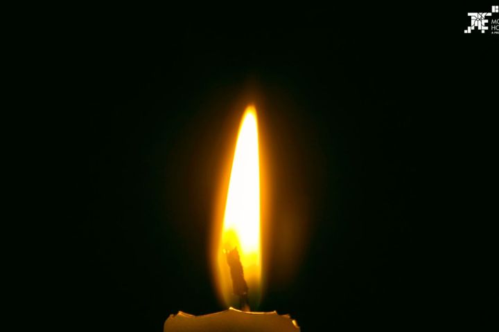 Single candle flame burning brightly in the dark.