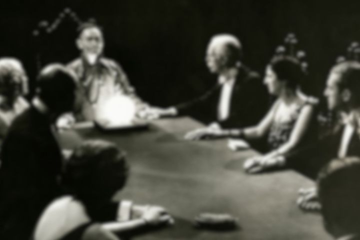 People seated around a table in a dimly lit room, focused on a glowing object.