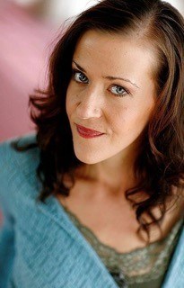 Woman with dark hair wearing a blue cardigan, smiling.