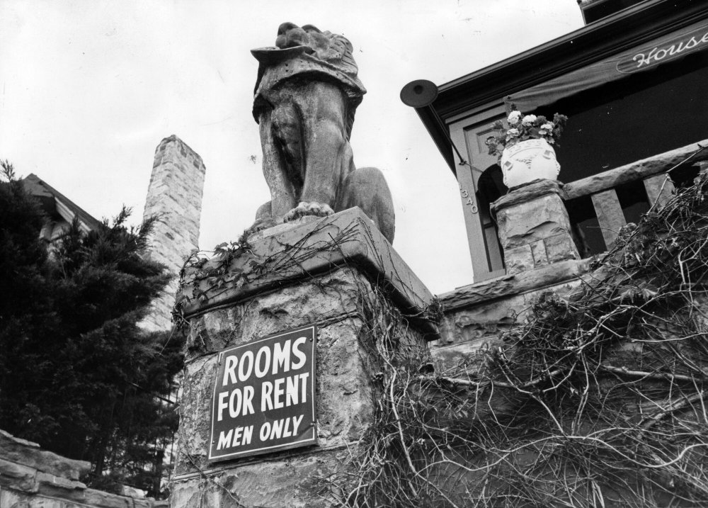 Stone lion statue on a porch with a sign: 'Rooms for Rent Men Only' below it.