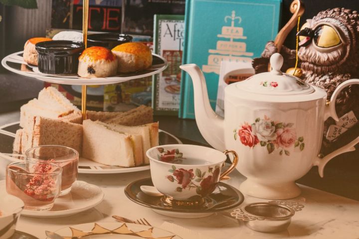 Afternoon tea set with scones, sandwiches, teapot, and owl figurine on a table.