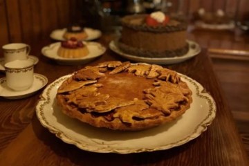 A pie with decorative crusts on a table, near cakes and teacups.