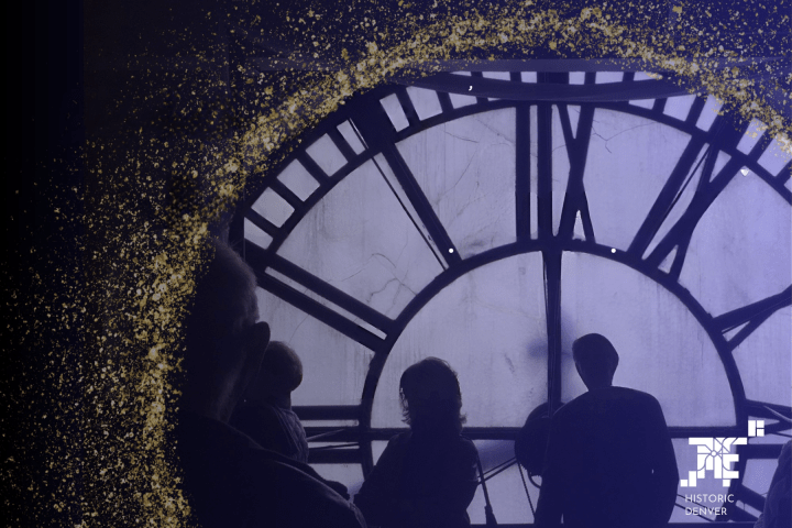 Silhouettes against large clock face with gold speckles in corner, Historic Denver logo visible.