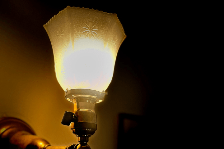 Lit lamp with a decorative frosted glass shade in a dark room.