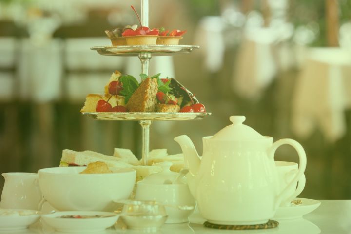 Afternoon tea setup with a teapot, cups, and a tiered tray of pastries and sandwiches.