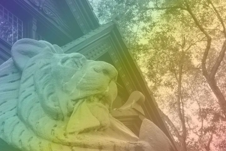 Statue of a lion head in rainbow light near trees.