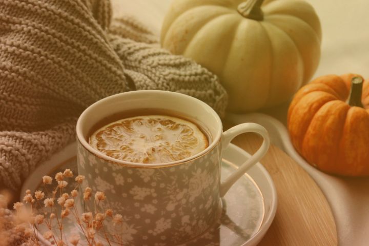 Tea with lemon slice in floral cup, sweater, and pumpkins on a tray.