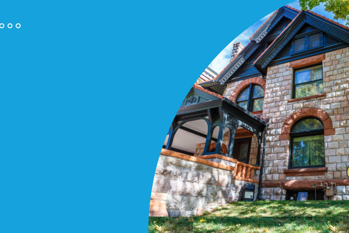 Large stone house with arched windows and wooden porch, blue sky background.