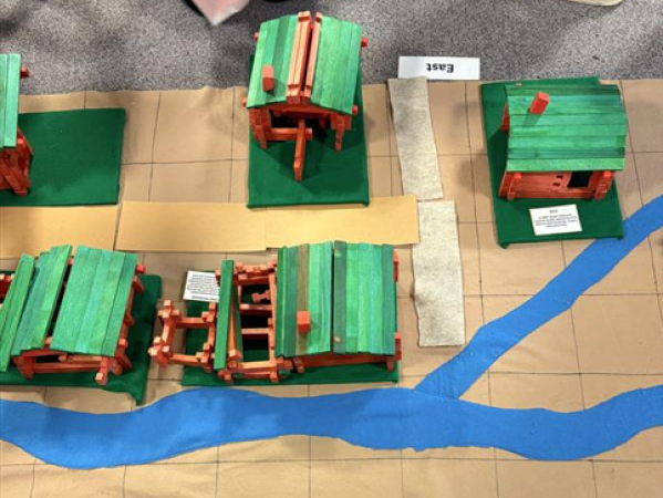 Miniature green-roofed log cabins on a map with blue river.