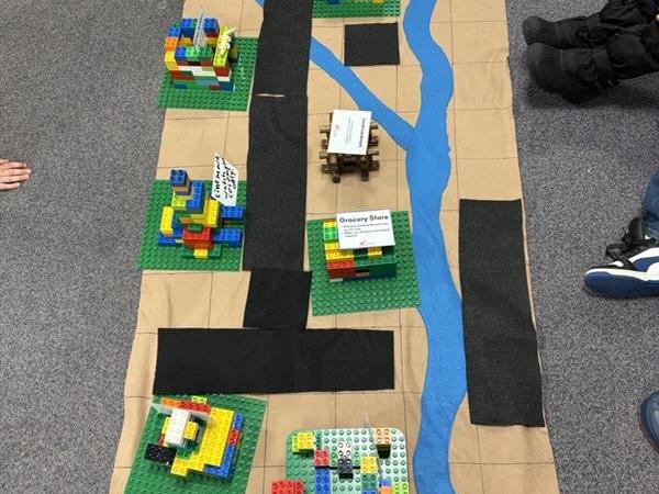 Colorful Lego models on a mat with a blue river and brown roads.